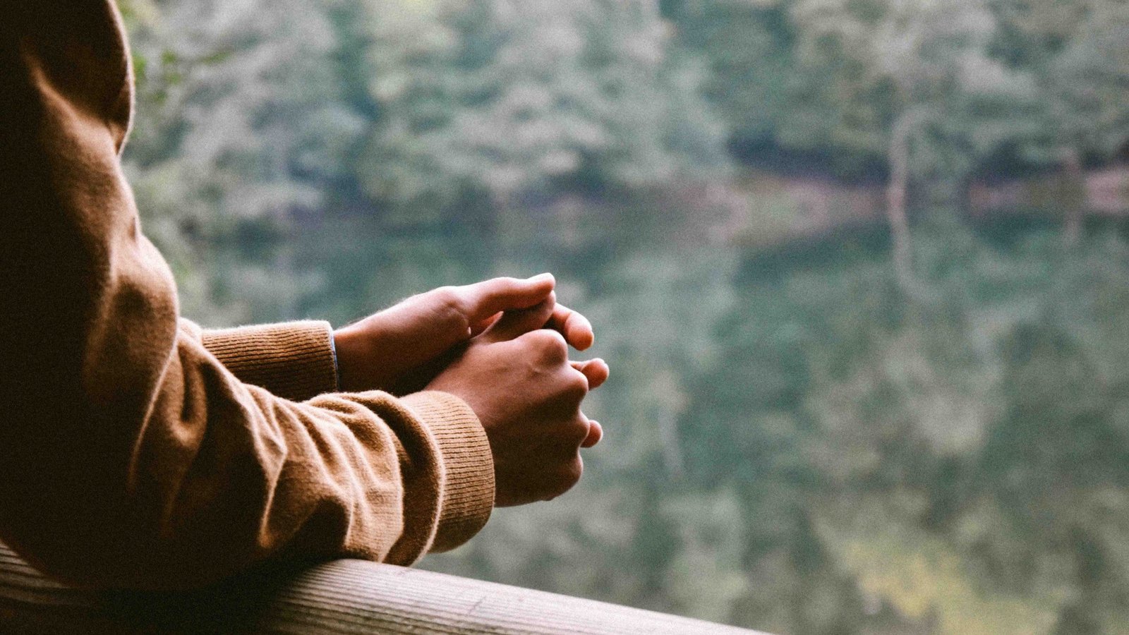 Person clasping hands while gazing at a calm lake, symbolizing quiet reflection and anxiety management